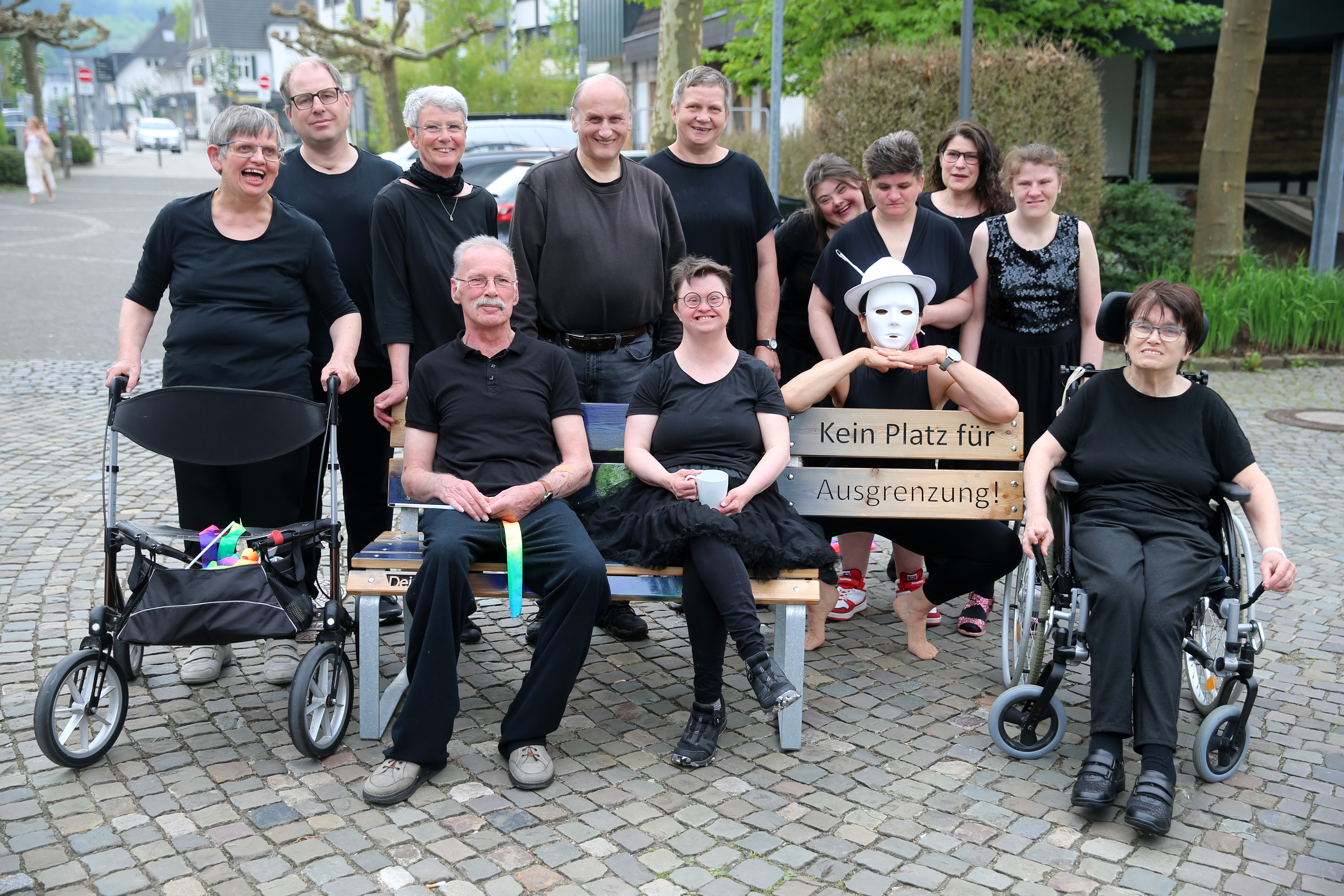 Eine Gruppe von Menschen, einige mit sichtbaren Behinderungen und Mobilitätshilfen, posiert im Freien mit einem Schild, auf dem "Kein Platz für Ausgrenzung" steht.