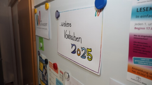 Ein Whiteboard mit verschiedenen Hinweisen und einem Schild mit der Aufschrift Weitere Vorhaben 2025 wird von Magneten gehalten.