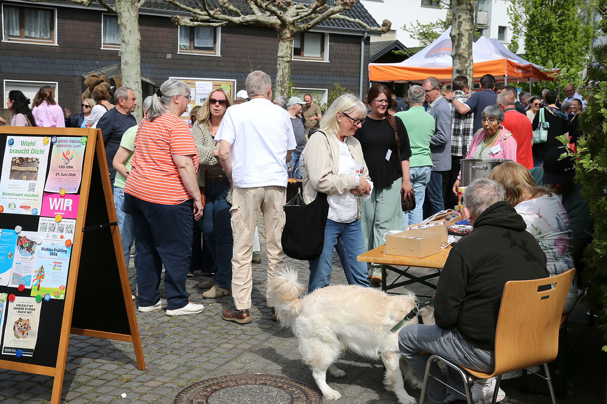 Menschen versammeln sich bei einer Veranstaltung im Freien mit Informationsständen, ausgestellten Flyern und einem Hund an der Leine im Vordergrund.