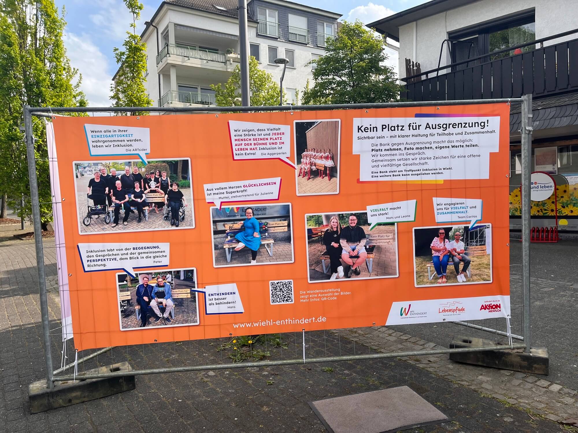 Ein orangefarbenes Banner mit deutschem Text und Fotos von Menschen, darunter auch Rollstuhlfahrer, das für Inklusion wirbt und sich gegen Ausgrenzung in der Gemeinschaft ausspricht.